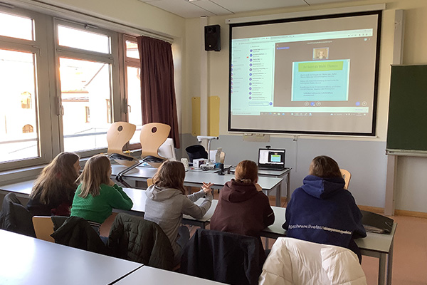Fünf Schülerinnen sitzen in einem Klassenzimmer und folgen einer Online-Konferenz.