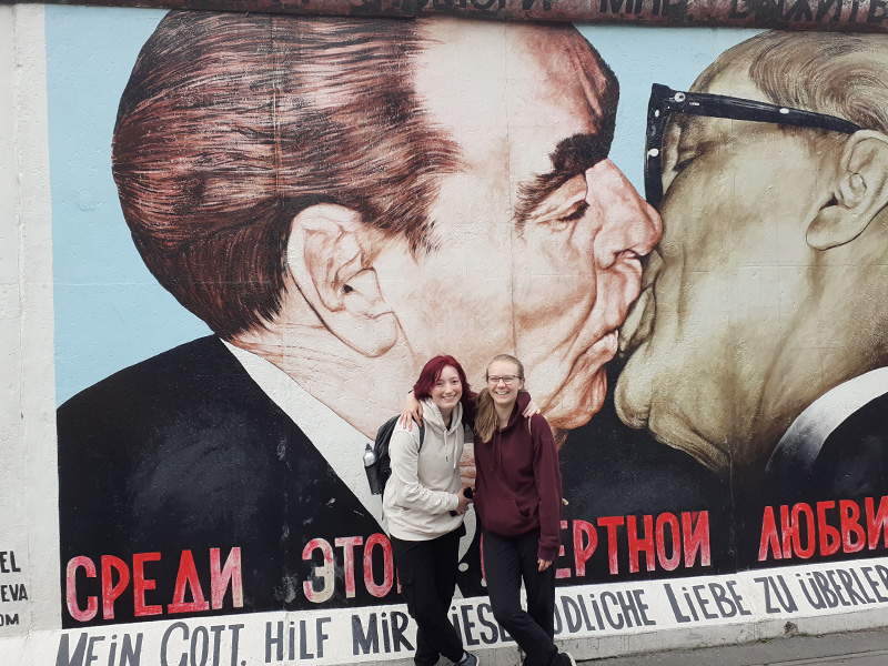 Zwei Schülerinnen stehen vor dem Bild "Mein Gott, hilf mir, diese tödliche Liebe zu überleben" der Berliner Mauer.