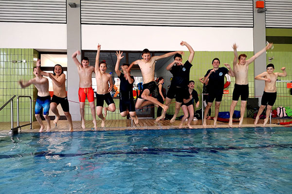 Schüler springen in lustigen Posen in ein Schwimmbecken.