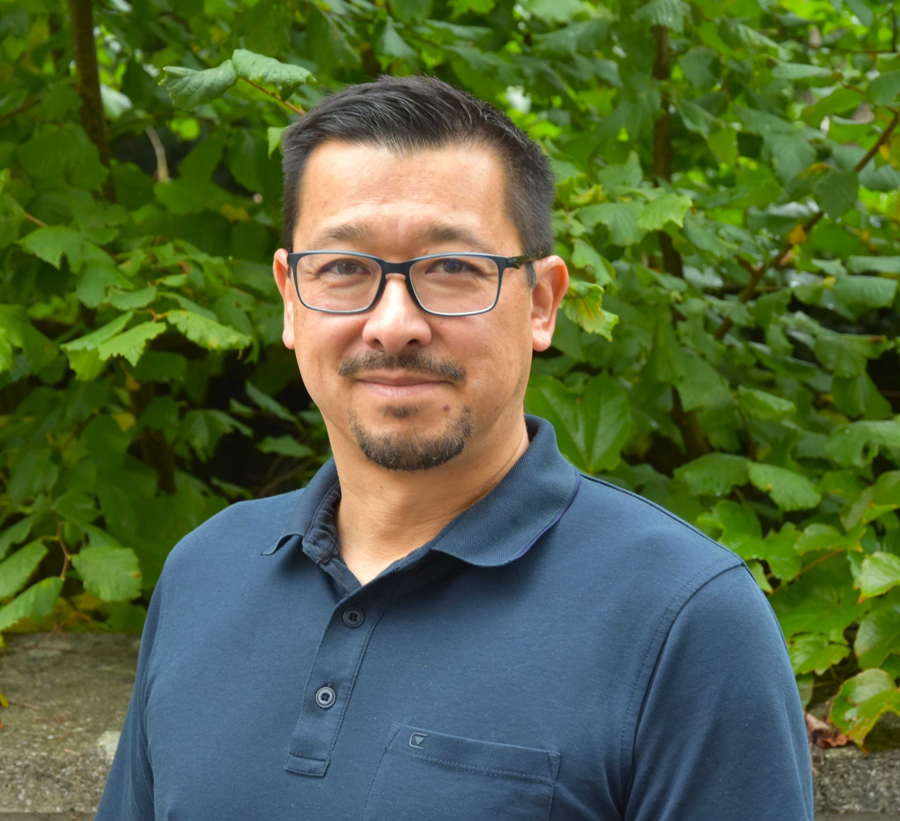 Porträt eines Mitarbeiters der Schulleitung, aufgenommen vor einem blauen Hintergrund.