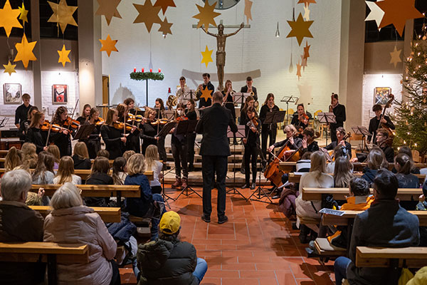 Zu sehen ist ein Kirchenraum, in dem das Sinfonieorchester spielt während davor Zuhörende in den Kirchenbänken sitzen.
