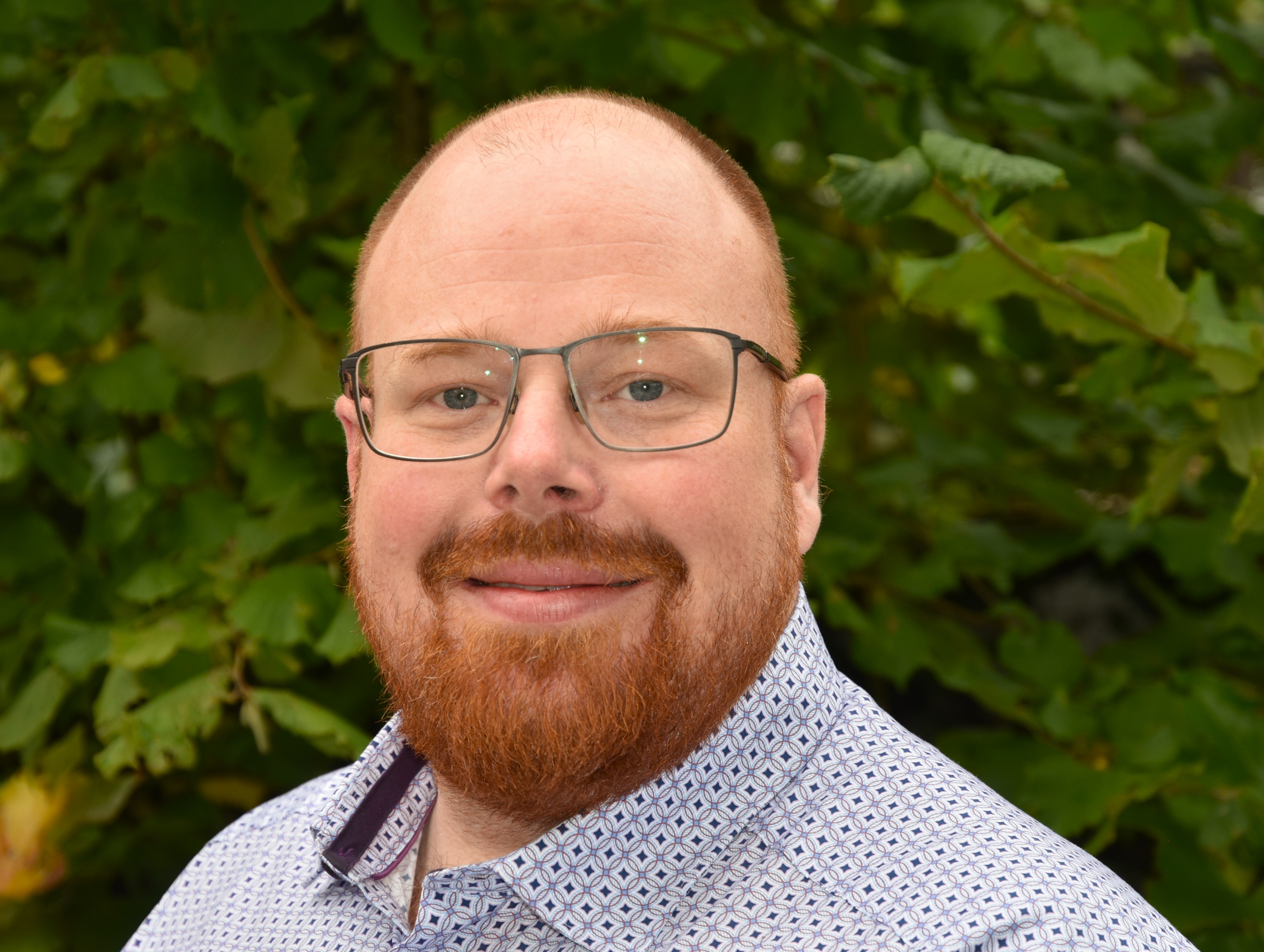 Porträt eines Mitarbeiters der Schulleitung, aufgenommen vor einem blauen Hintergrund.