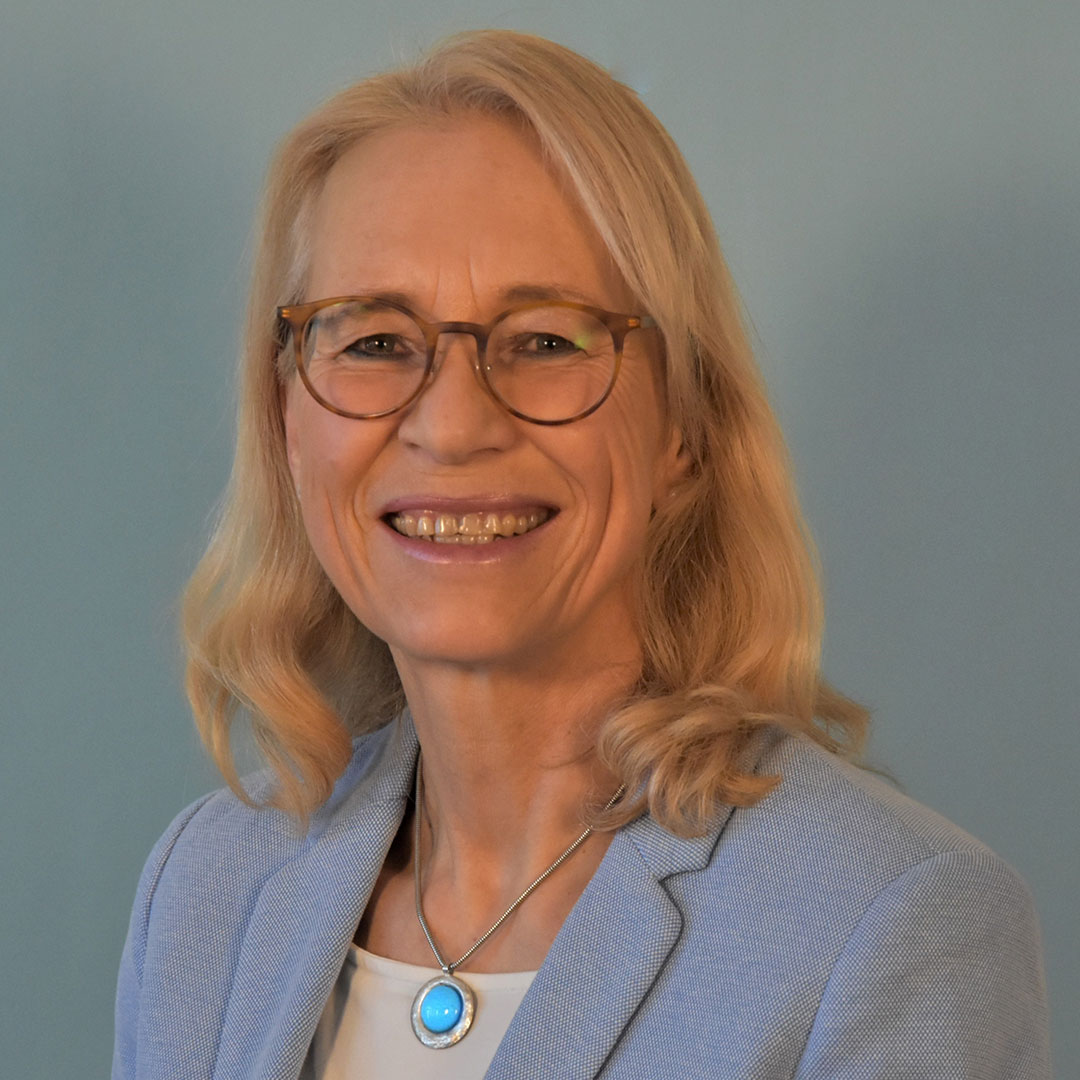 Porträt einer Mitarbeiterin der Schulleitung, aufgenommen vor einem blauen Hintergrund.