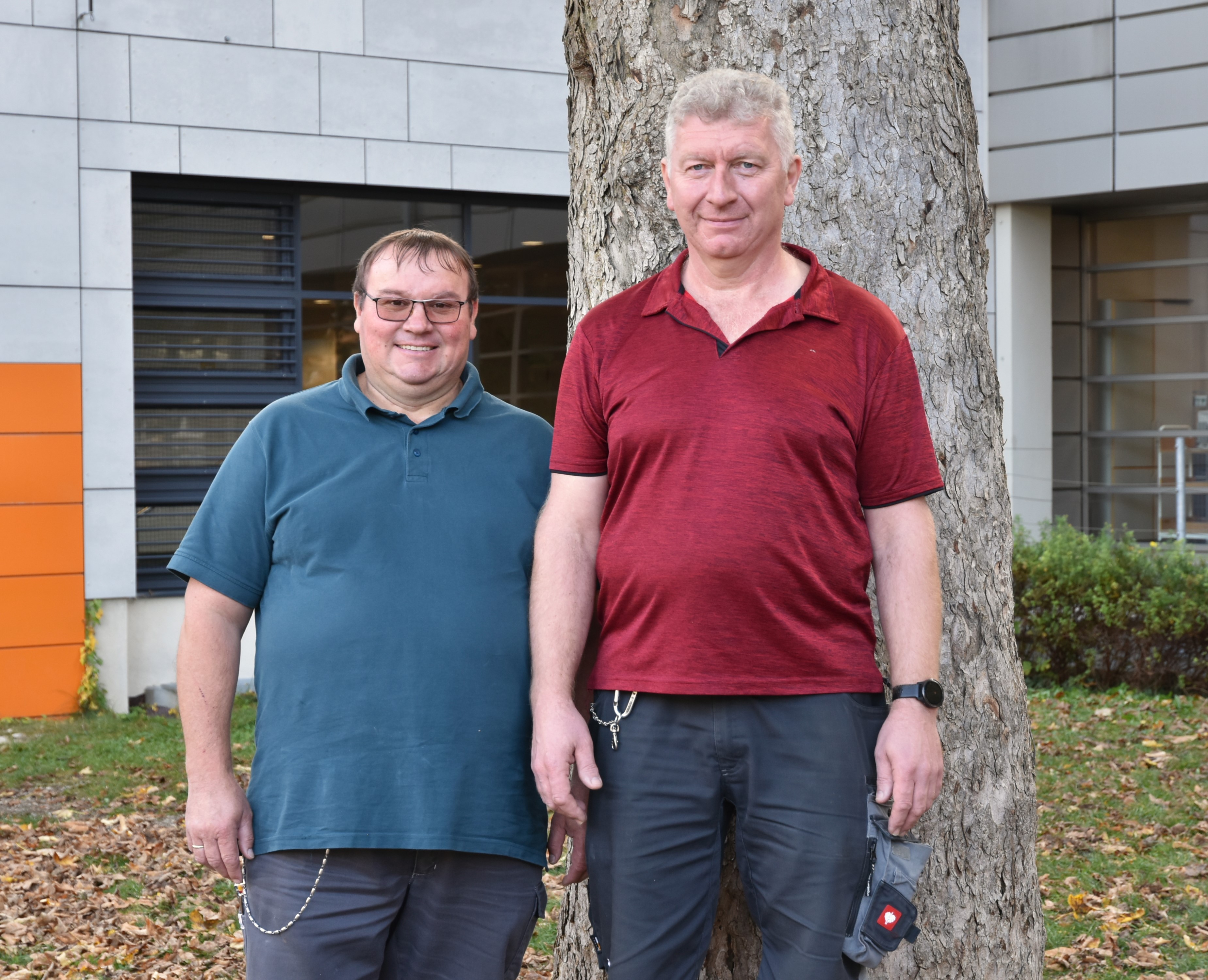 Die beiden Hausmeister der Schule stehen im Schulgarten vor einem Baum.