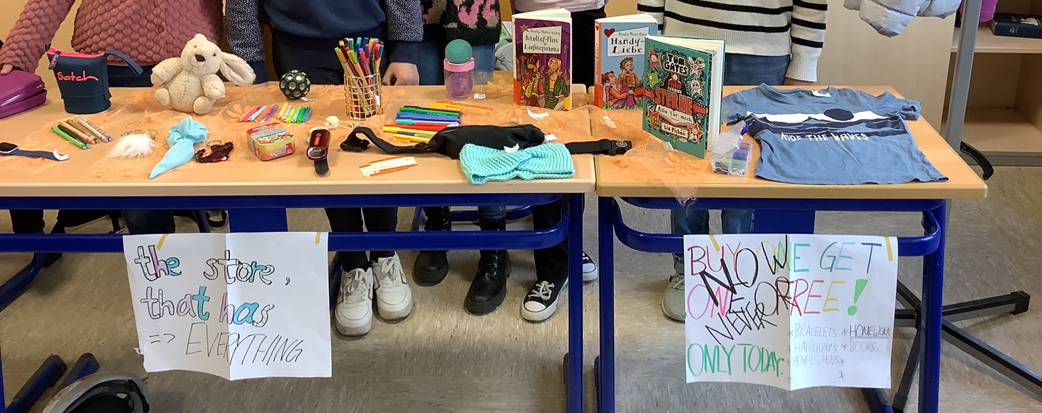 Zu sehen ist ein Flohmarktstand hinter dem Kinder stehen.