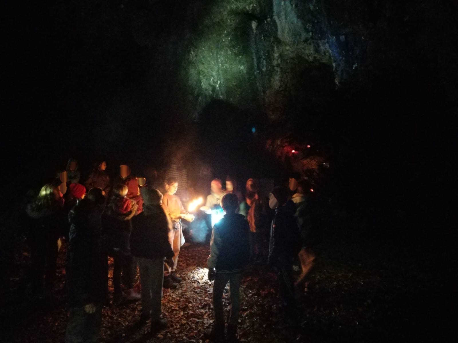 Zu sehen sind Schülerinnen und Schüler im Dunkeln mit Fackeln in der Hand vor einer beleuchteten Grotte.