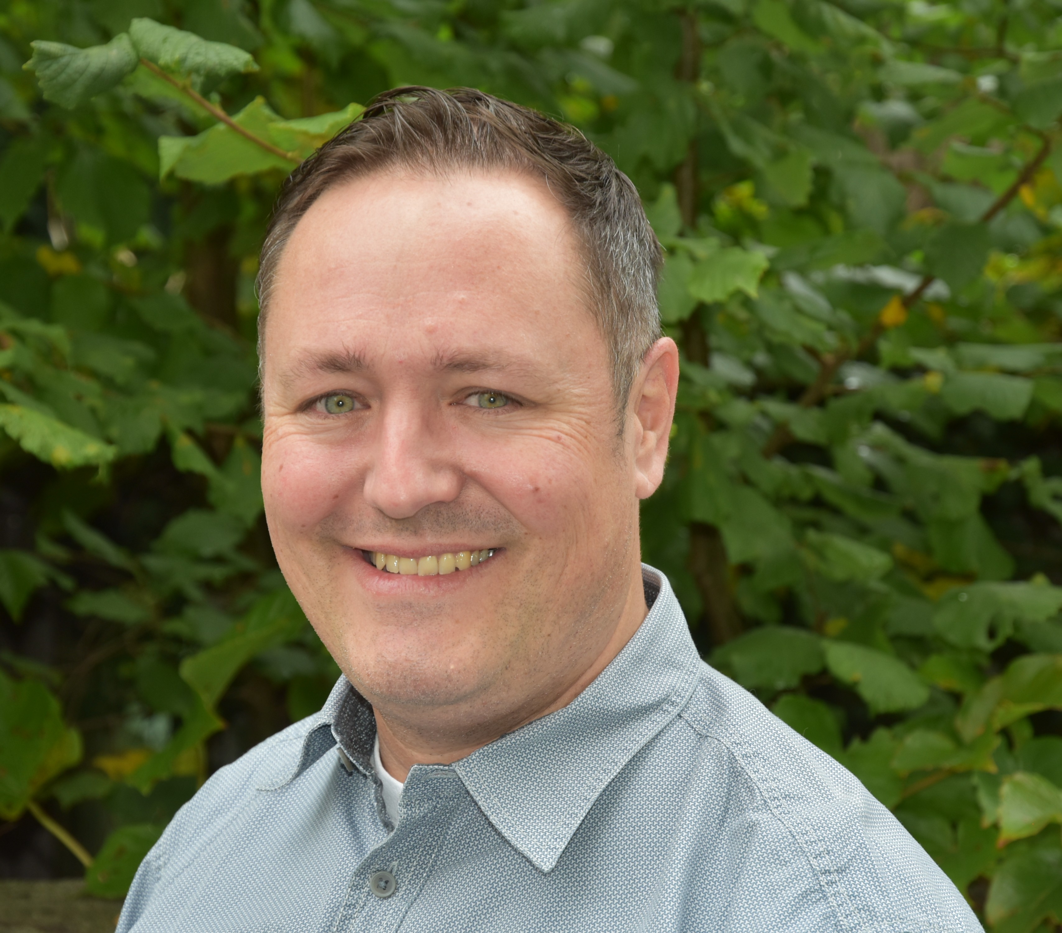 Porträt eines Mitarbeiters der Schulleitung, aufgenommen vor einem blauen Hintergrund.