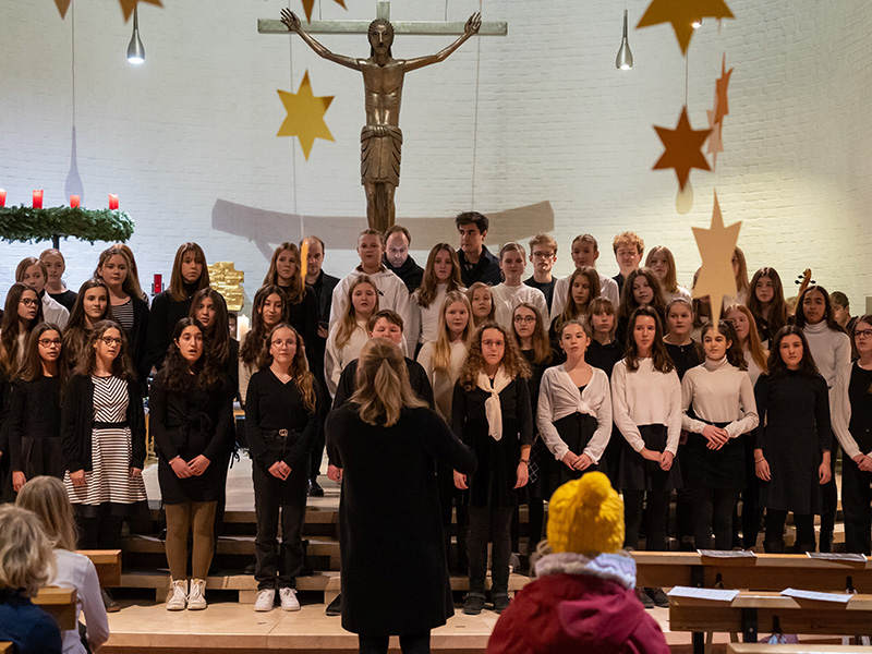 Schülerinnen und Schüler des Mittelstufenchors singen in einer Kirche.  Vor ihnen steht ihre Dirigenten.