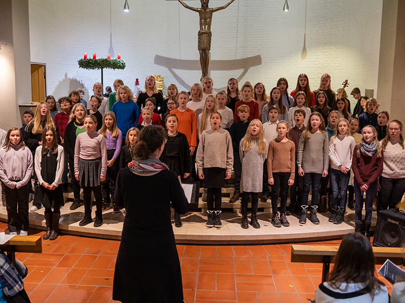 Zu sehen sind Kinder, die in einer Kirche sind. Vor ihnen steht ihre Dirigentin.