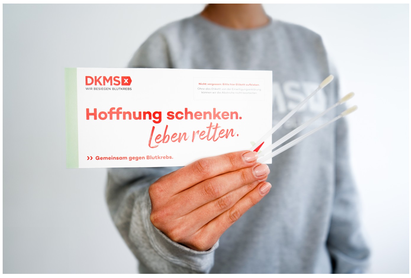 Zu sehen ist eine Person, die ein DKMSdokument mit dem Titel "Hoffnung schenken. Leben retten." hält.