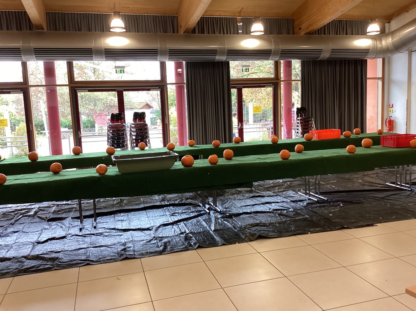 Zu sehen ist die Aula des Gymnasiums. Auf langen Tischen sind grüne Filztischdecken gelegt, auf denen Kürbisse stehen.