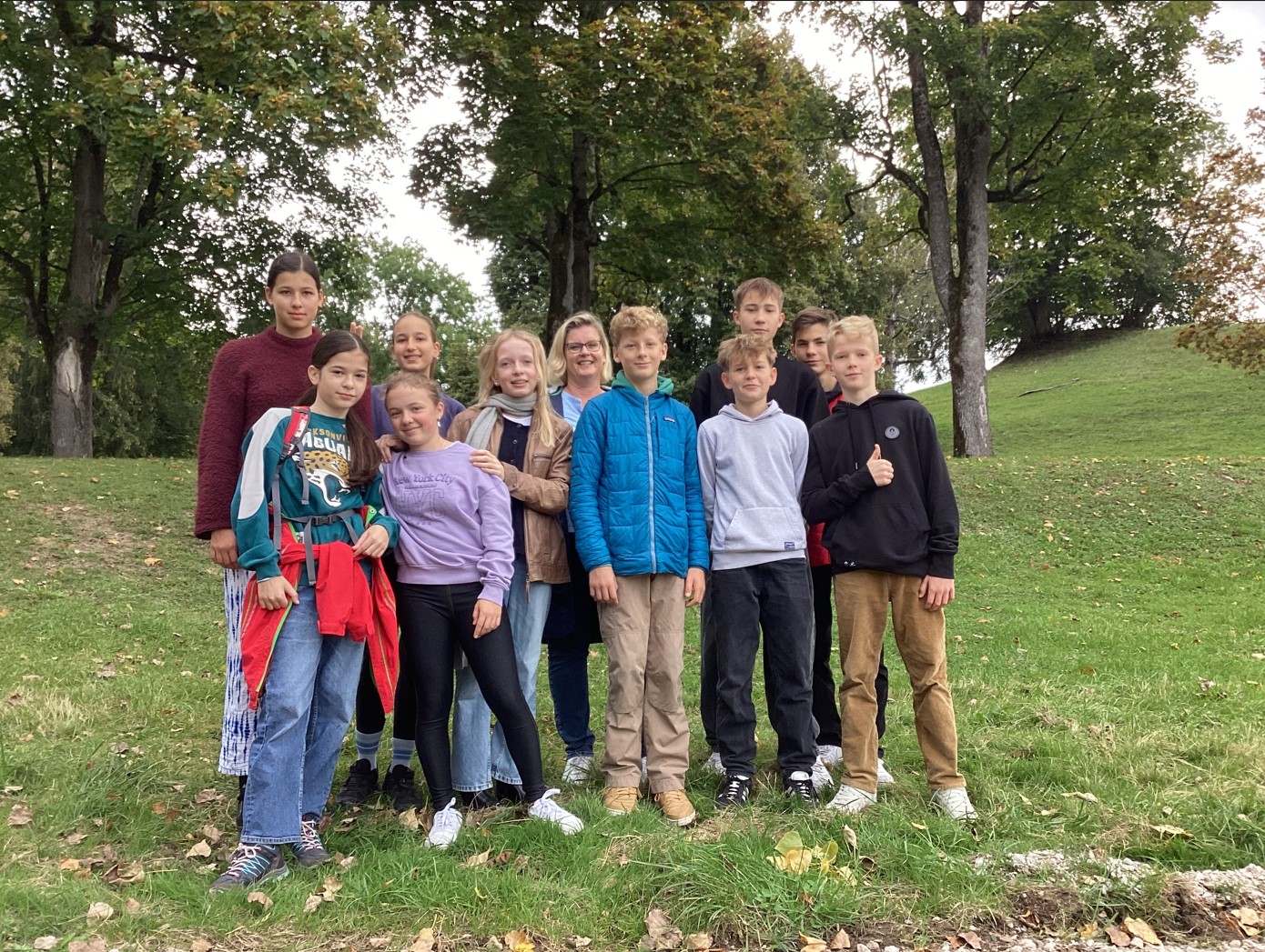 Schülerinnen und Schüler stehen auf einem grünen Hang mit Bäumen und blicken in die Kamera.
