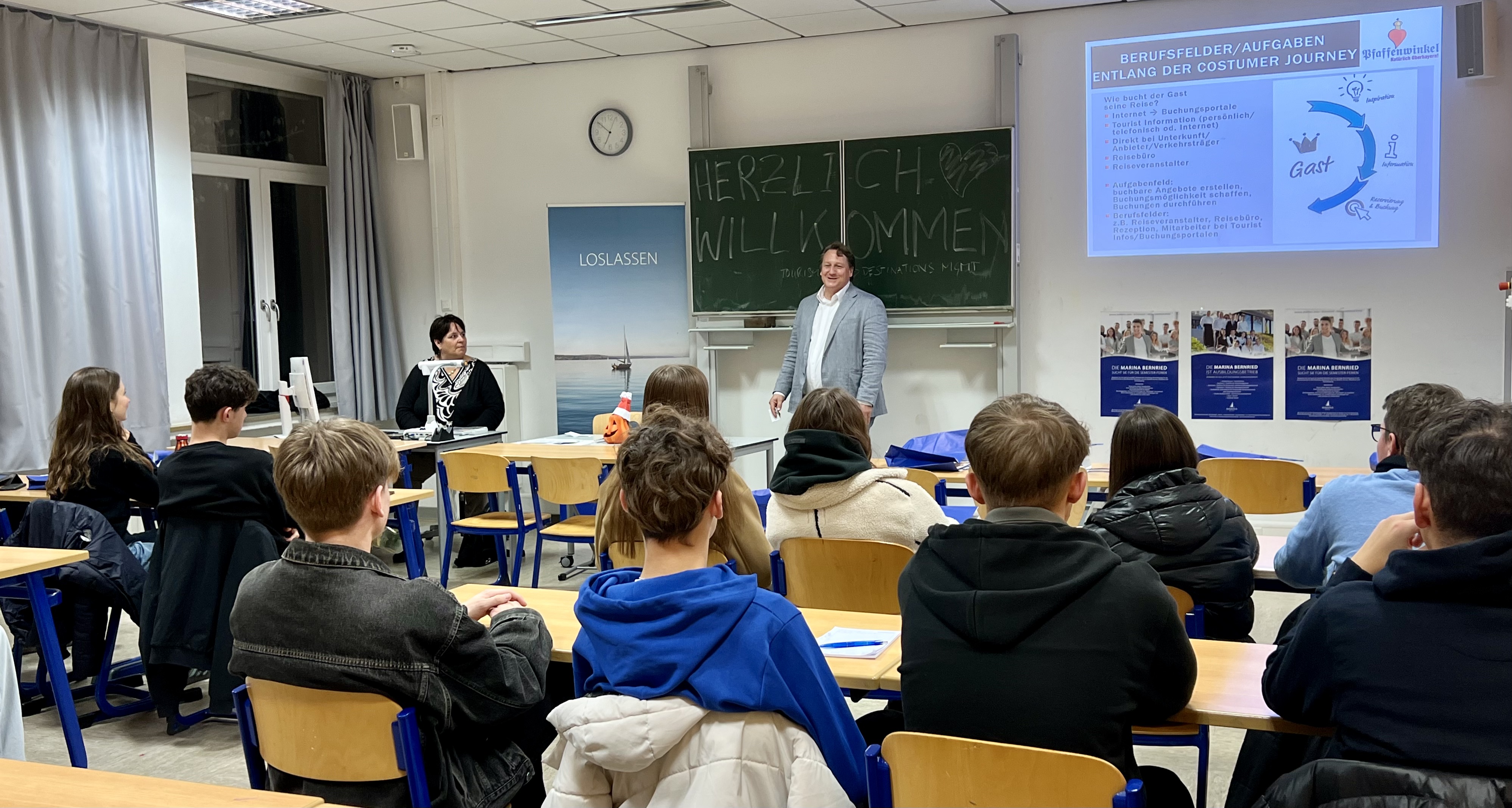 Vertretende des Rotari-Clubs präsentieren Berufsfelder und Aufgaben in einem Klassenzimmer. Schülerinnen und Schüler sitzen in den Schulbänken und hören zu.
